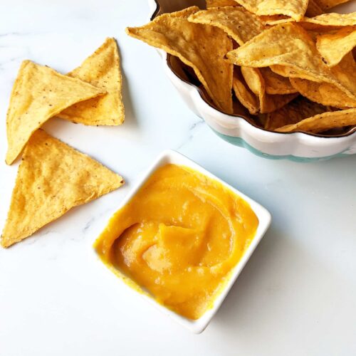 A tiny bowl of vegan nacho cheese sauce next to a bowl of tortilla chips.