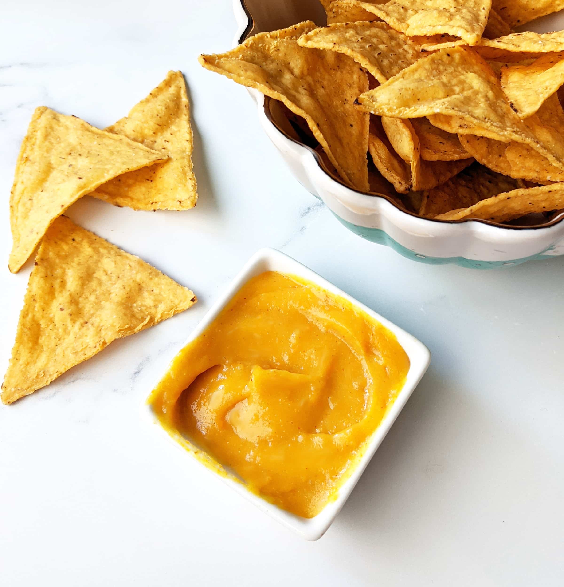 A tiny bowl of vegan nacho cheese sauce next to a bowl of tortilla chips.