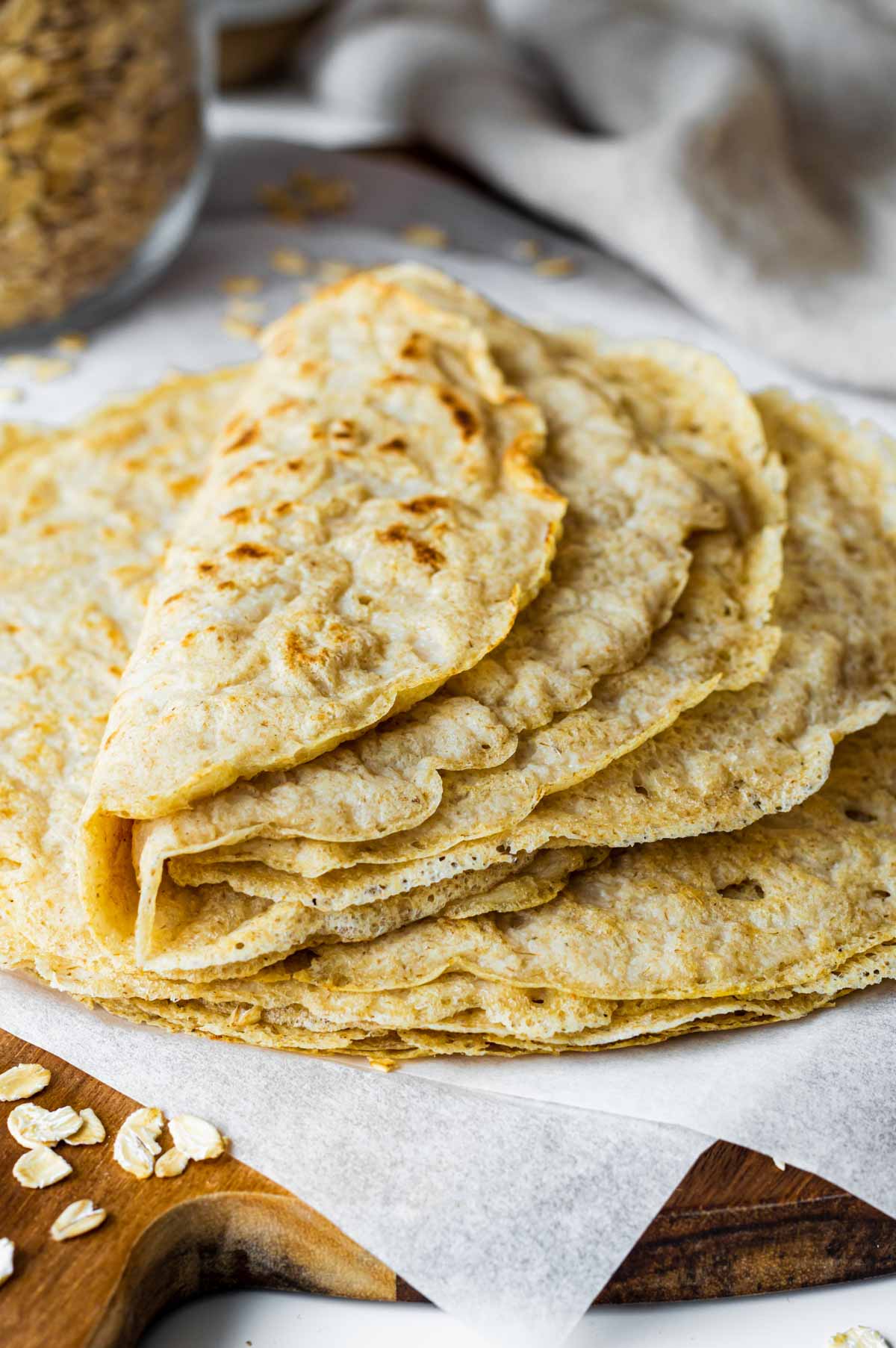 Folded oat tortillas served on a round wooden board layered with parchment paper.