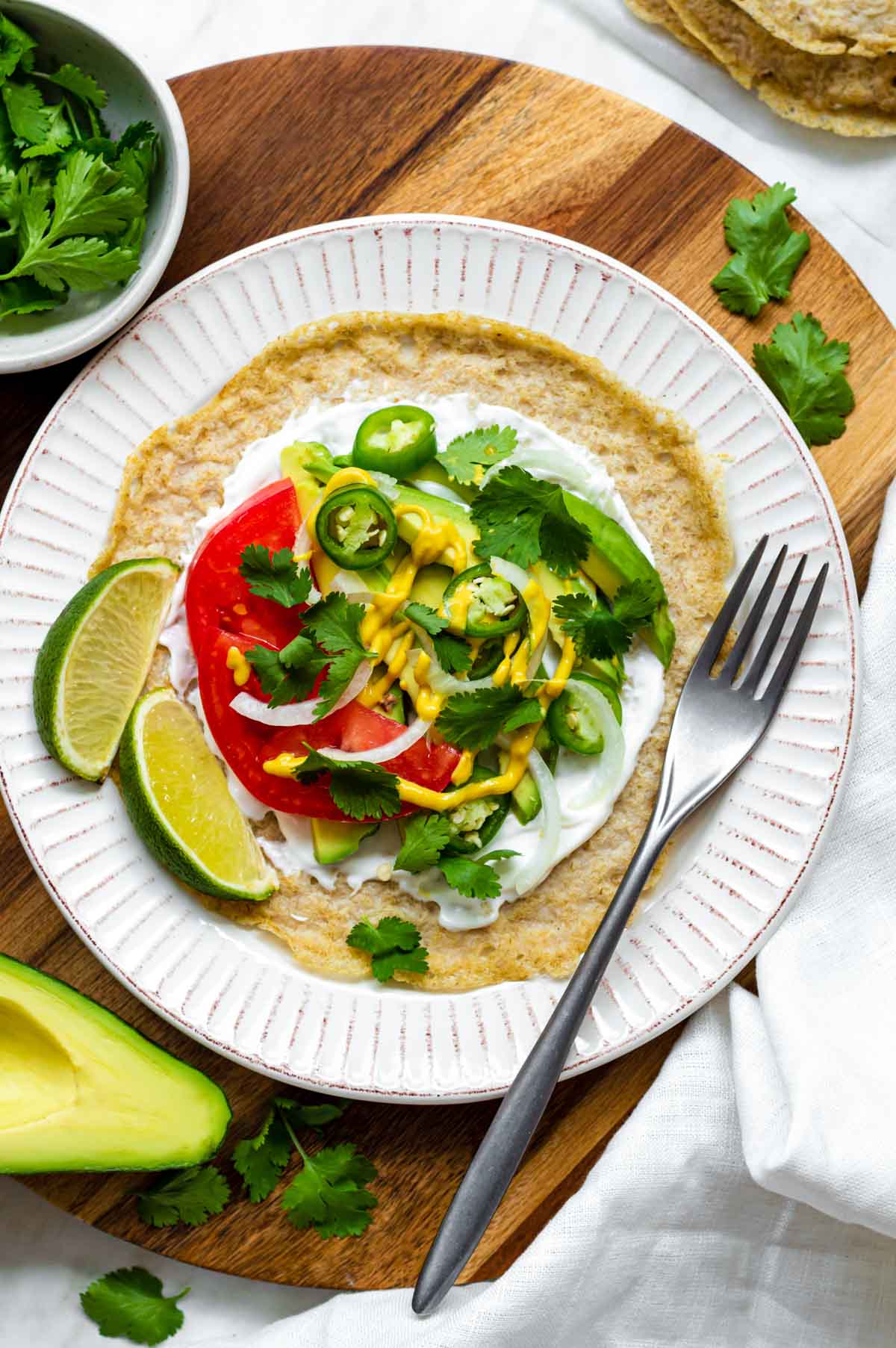Oat tortilla served on a white plate and filled with vegan mayo, avocado, tomatoes and cilantro.