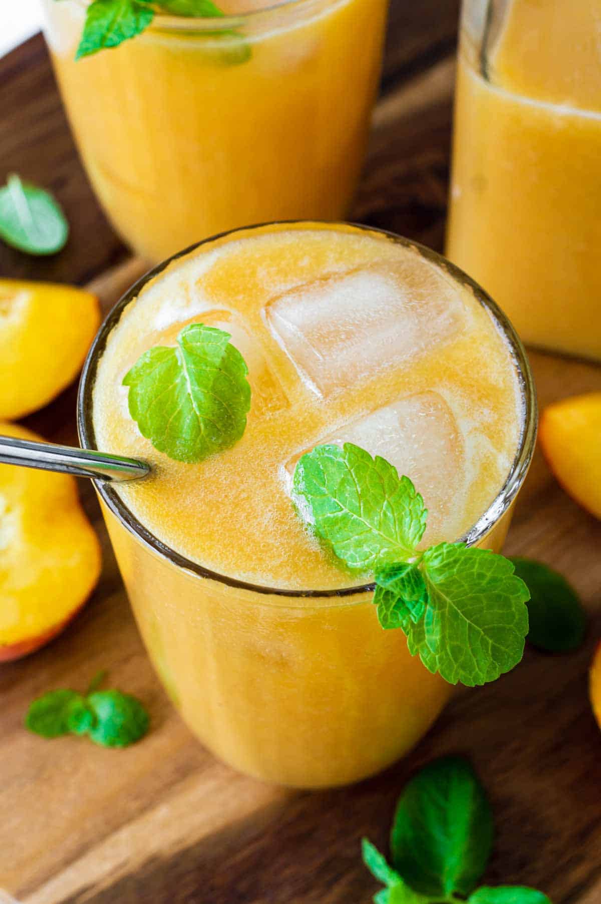 Peach juice served in a glass and topped with ice cubes and fresh mint.
