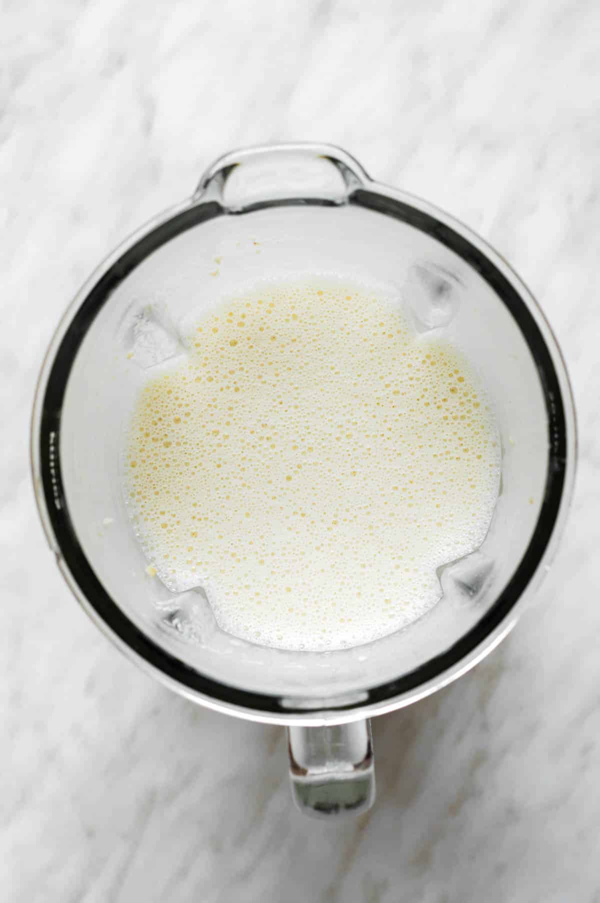 A mixture of cashews, coconut cream and nutritional yeast in a blender.