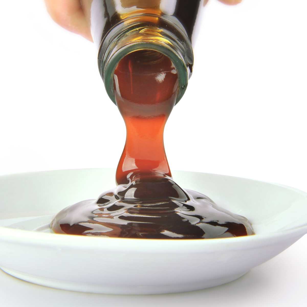 Hand pouring vegan oyster sauce out of a bottle into a bowl.