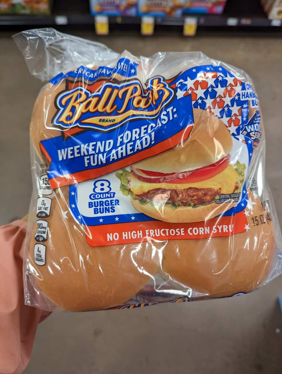 An arm holding up a package of Ball Park hamburger buns.