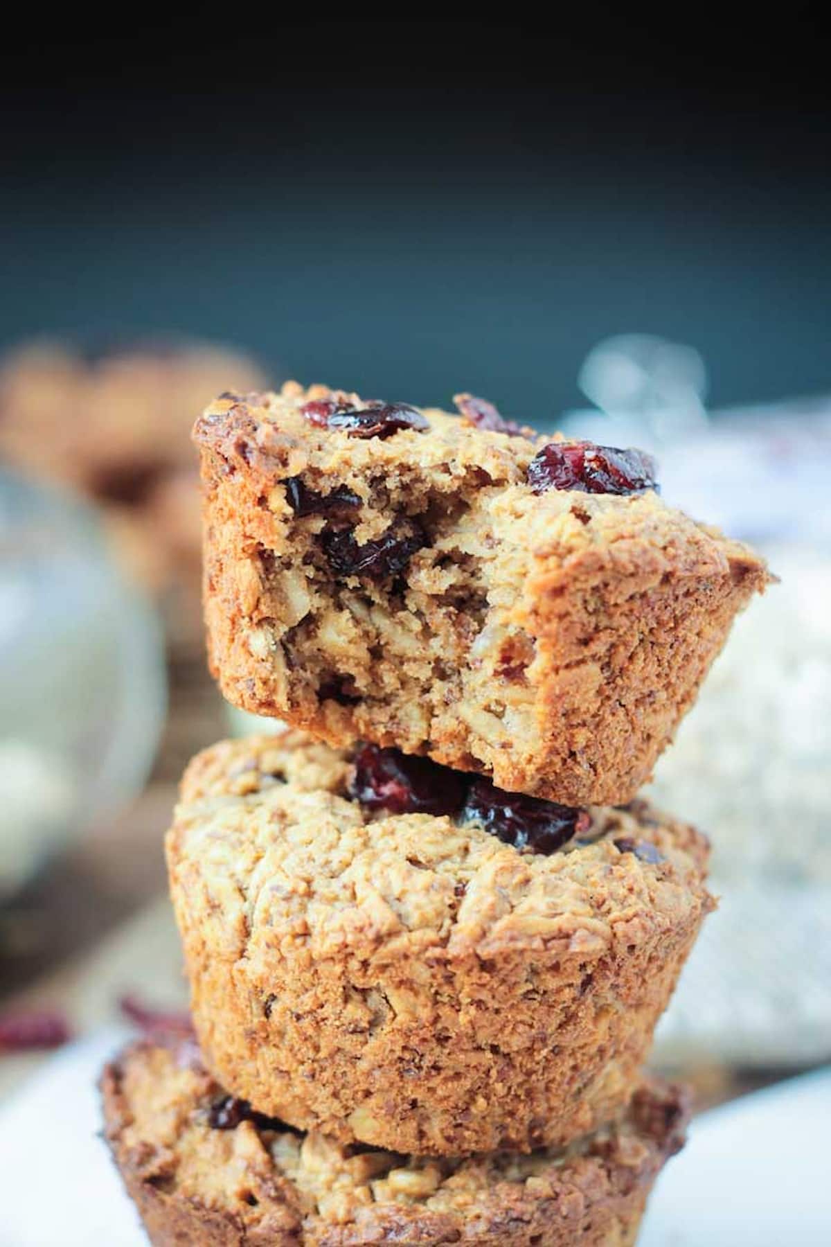 Three baked cranberry oatmeal muffins stacked with the top one missing a bite.