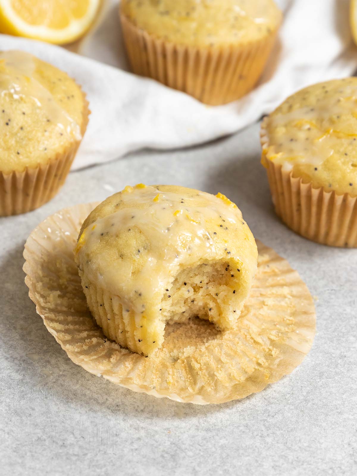 Vegan lemon poppyseed muffin sitting on a muffin line with a bite missing.