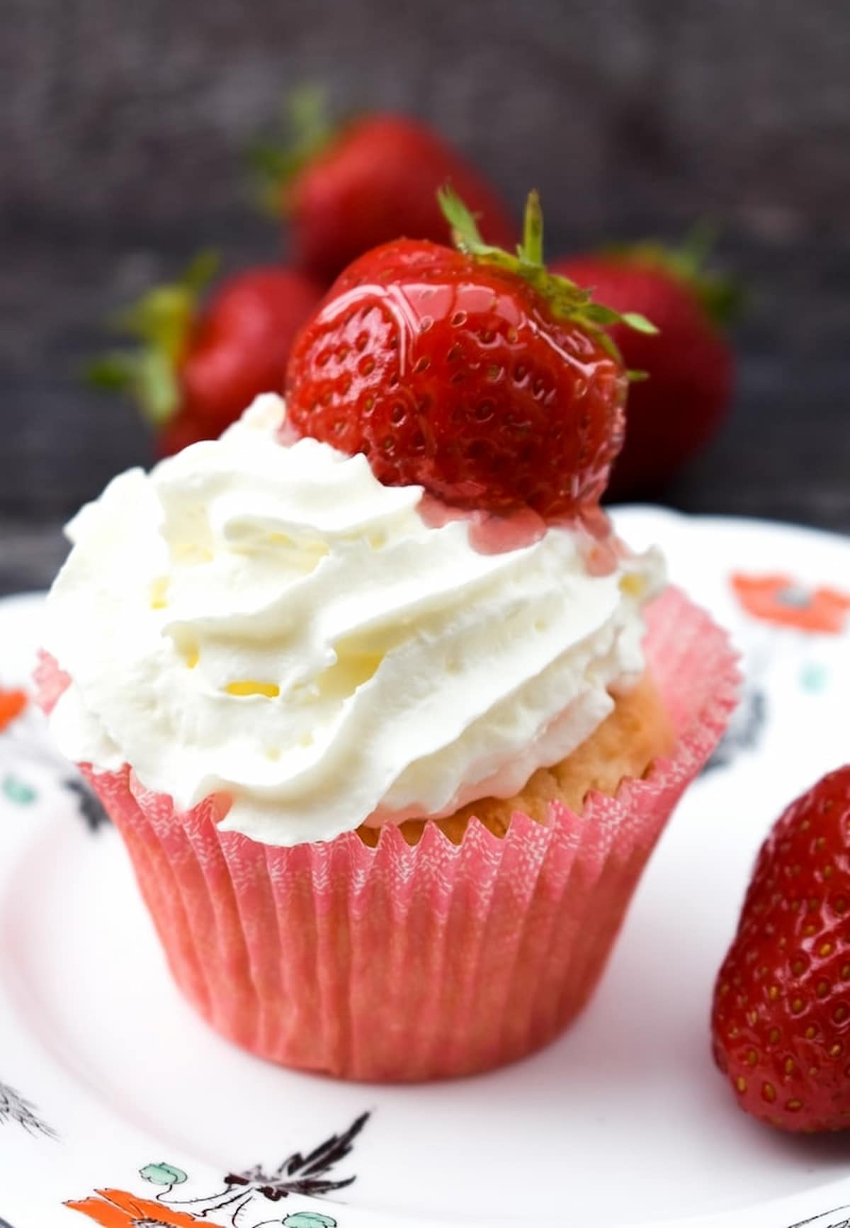 Vegan strawberry cupcakes topped with vegan whipped cream and a fresh strawberry.