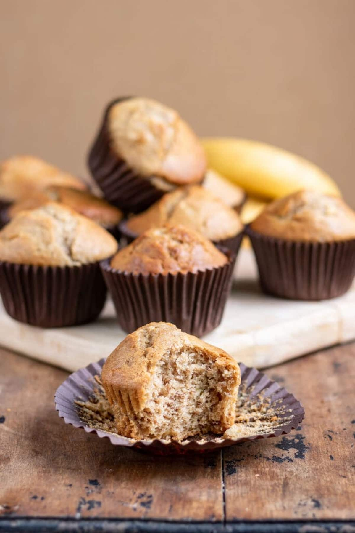 Vegan banana muffin sitting in it's pan liner with a bite missing.