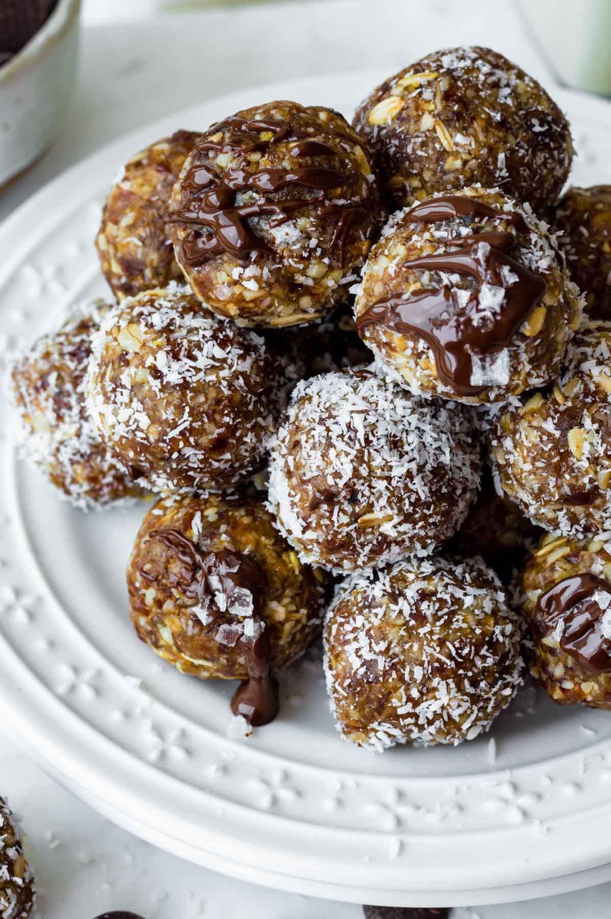 A white plate filled with energy balls. Some of them are drizzled with melted chocolate and sprinkled with flaky salt.