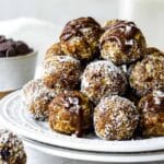 Bliss balls stacked on top of each other topped with melted chocolate and sea salt.