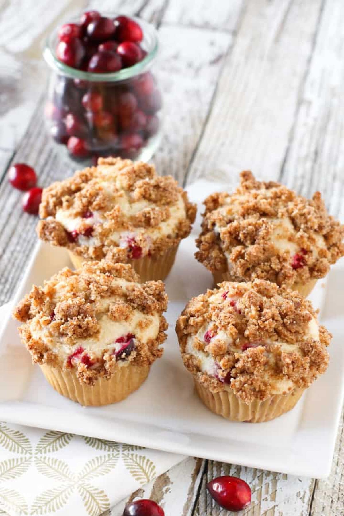 Four vegan cranberry coffee cake muffins on a plate, topped with a cinnamon crumb topping.