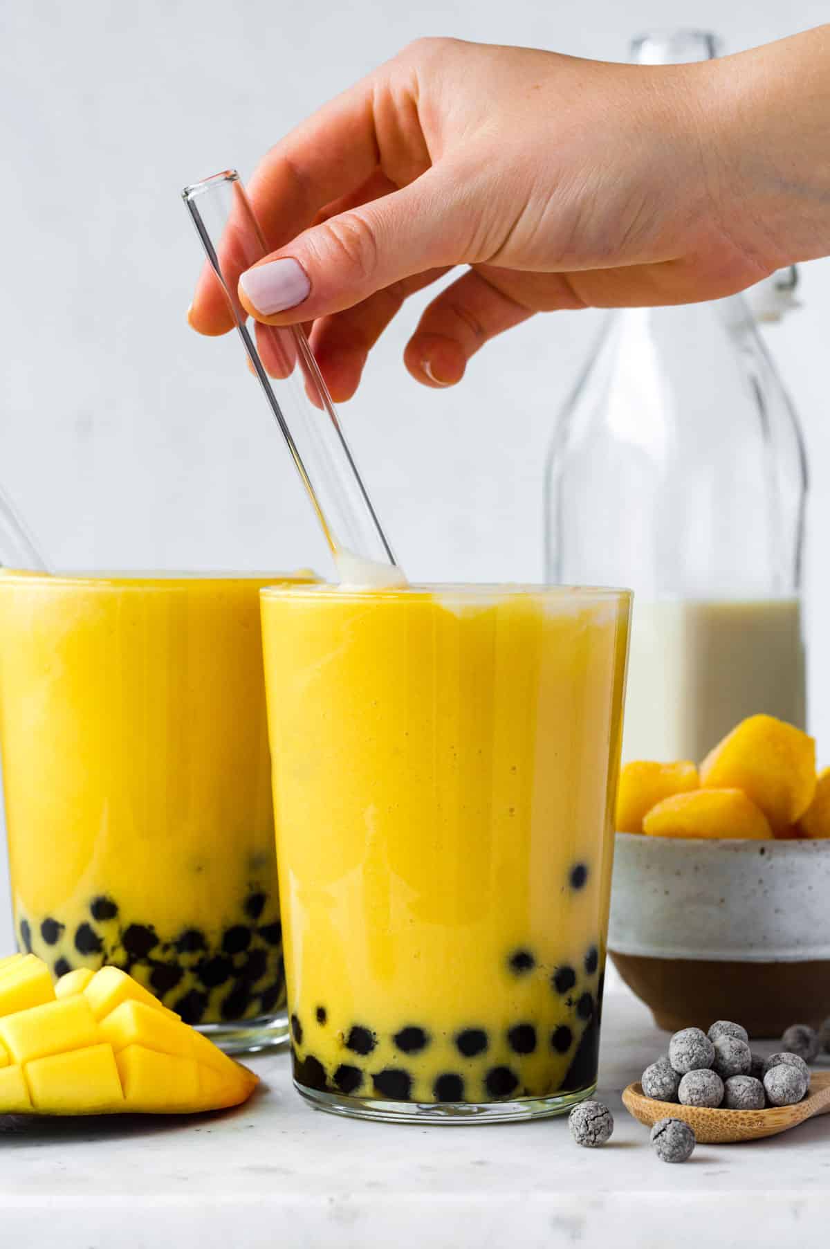 A hand placing a boba straw into a glass full of bubble milk tea.