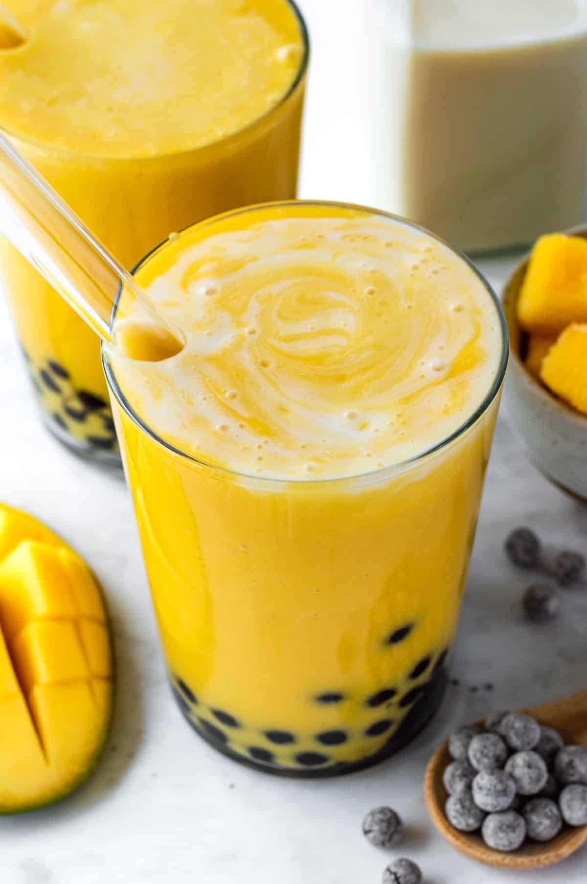 A glass filled with mango bubble tea, with a glass straw pointing out of them.