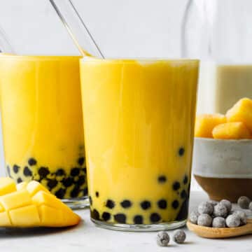 Two glasses of mango bubble tea with boba straws pointing out of them.