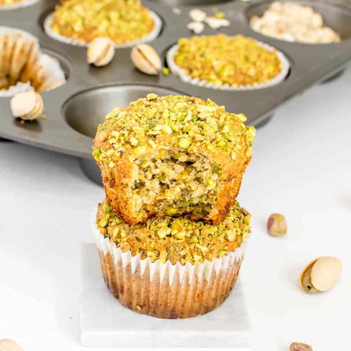 Two pistachio muffins stacked with the top muffin missing a bite out of it.