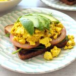 Silken tofu scramble served on toast with spinach, tomatoes, and sliced avocado.