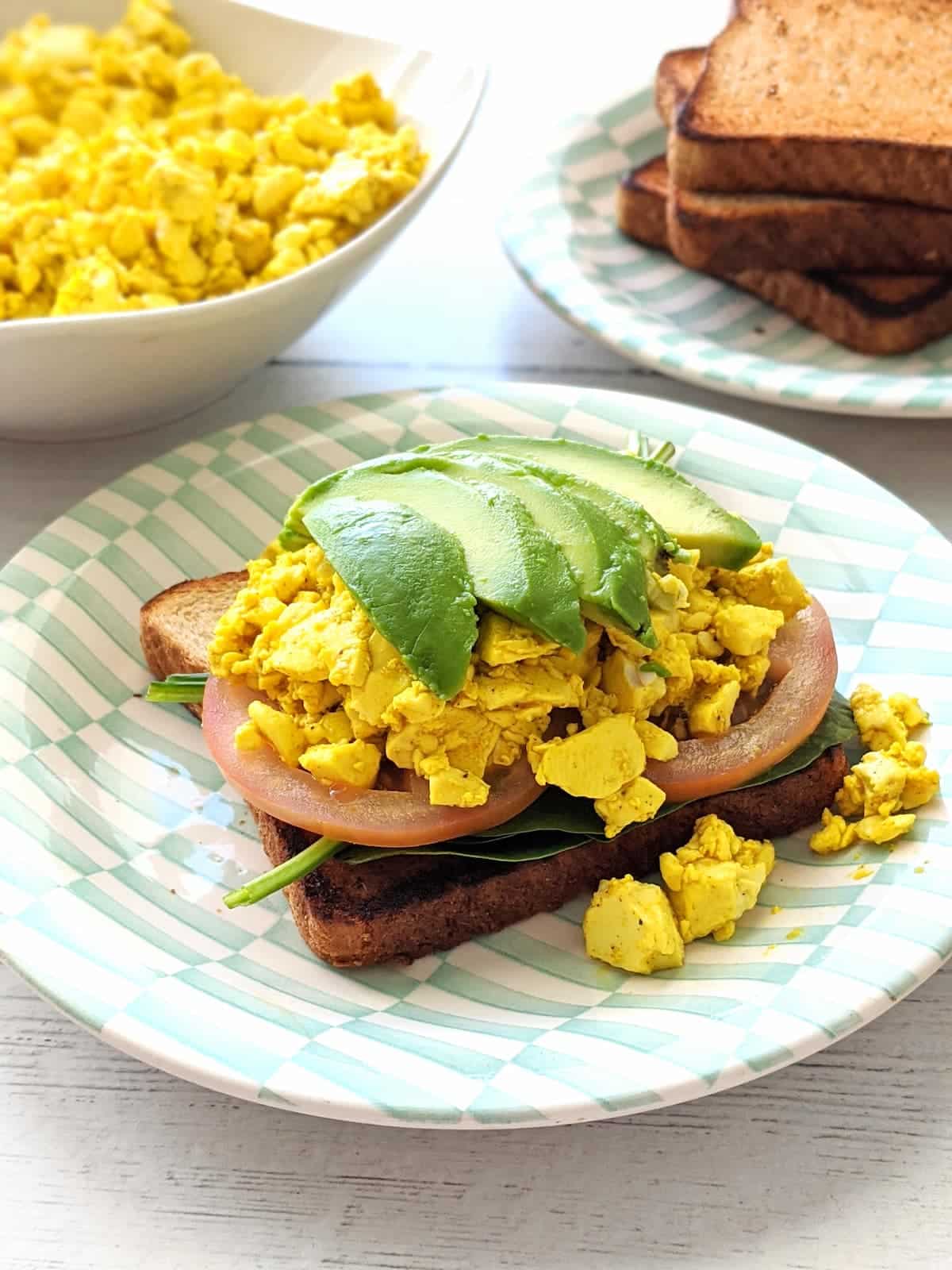 Silken tofu scramble served on toast with spinach, tomatoes, and sliced avocado.