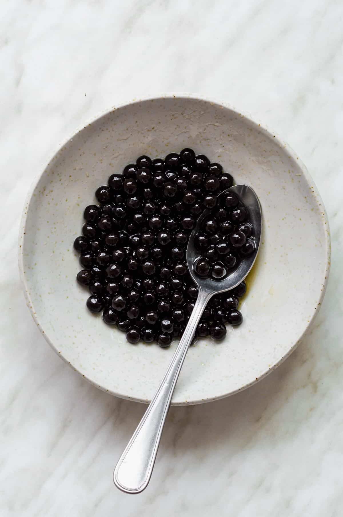 Cooked tapioca pearls coated in maple syrup, served in a white bowl with a spoon in it.