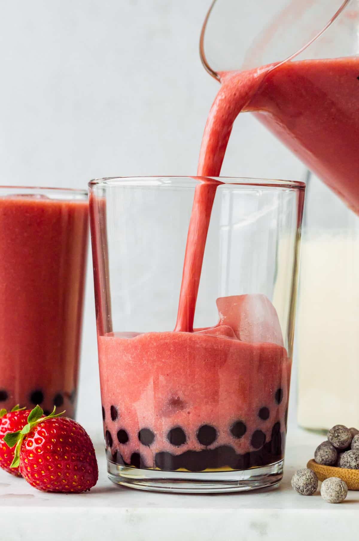 Pouring strawberry smoothie over boba pearls in a glass.