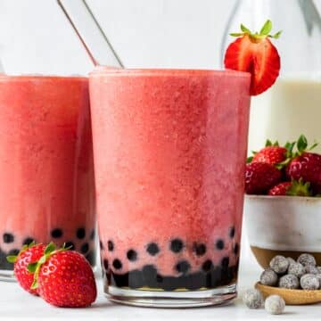 Two glasses of strawberry bubble tea with boba straws pointing out of them.