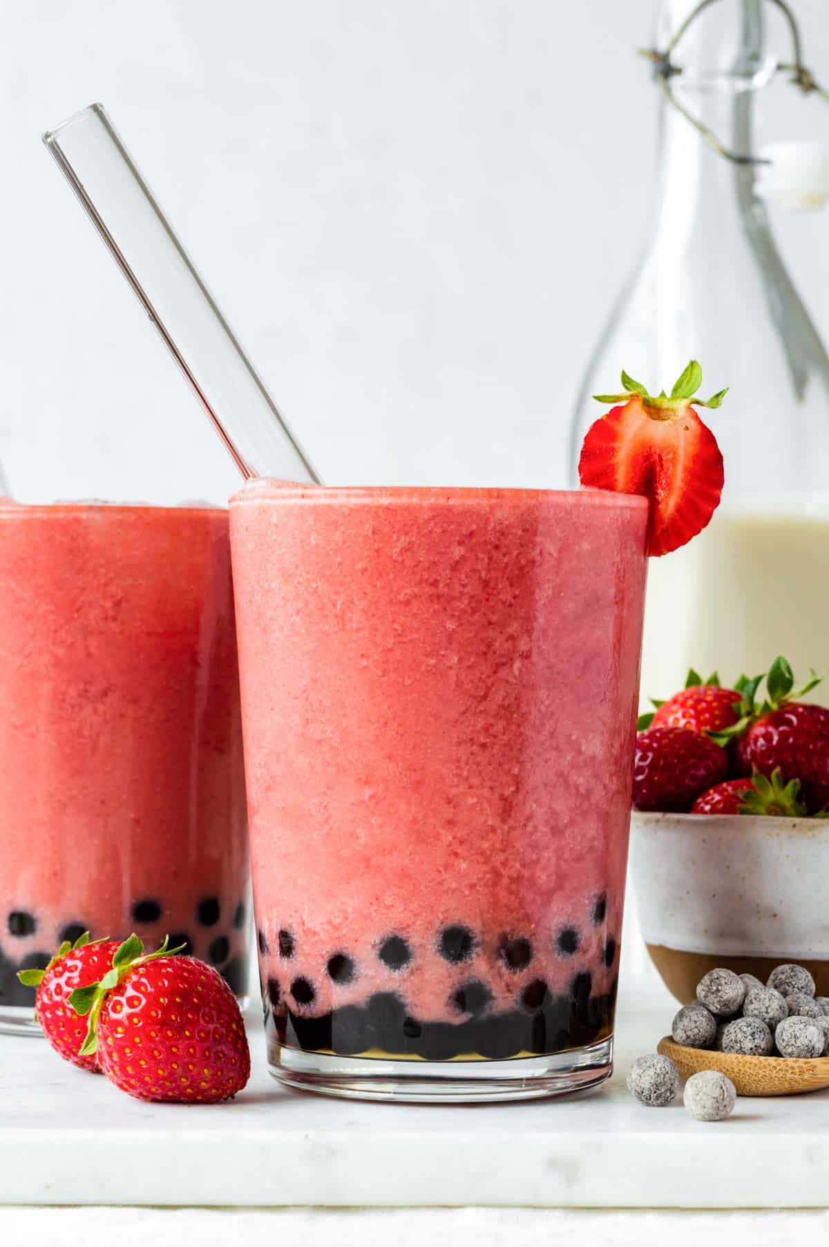 Two glasses of strawberry bubble tea with boba straws pointing out of them.