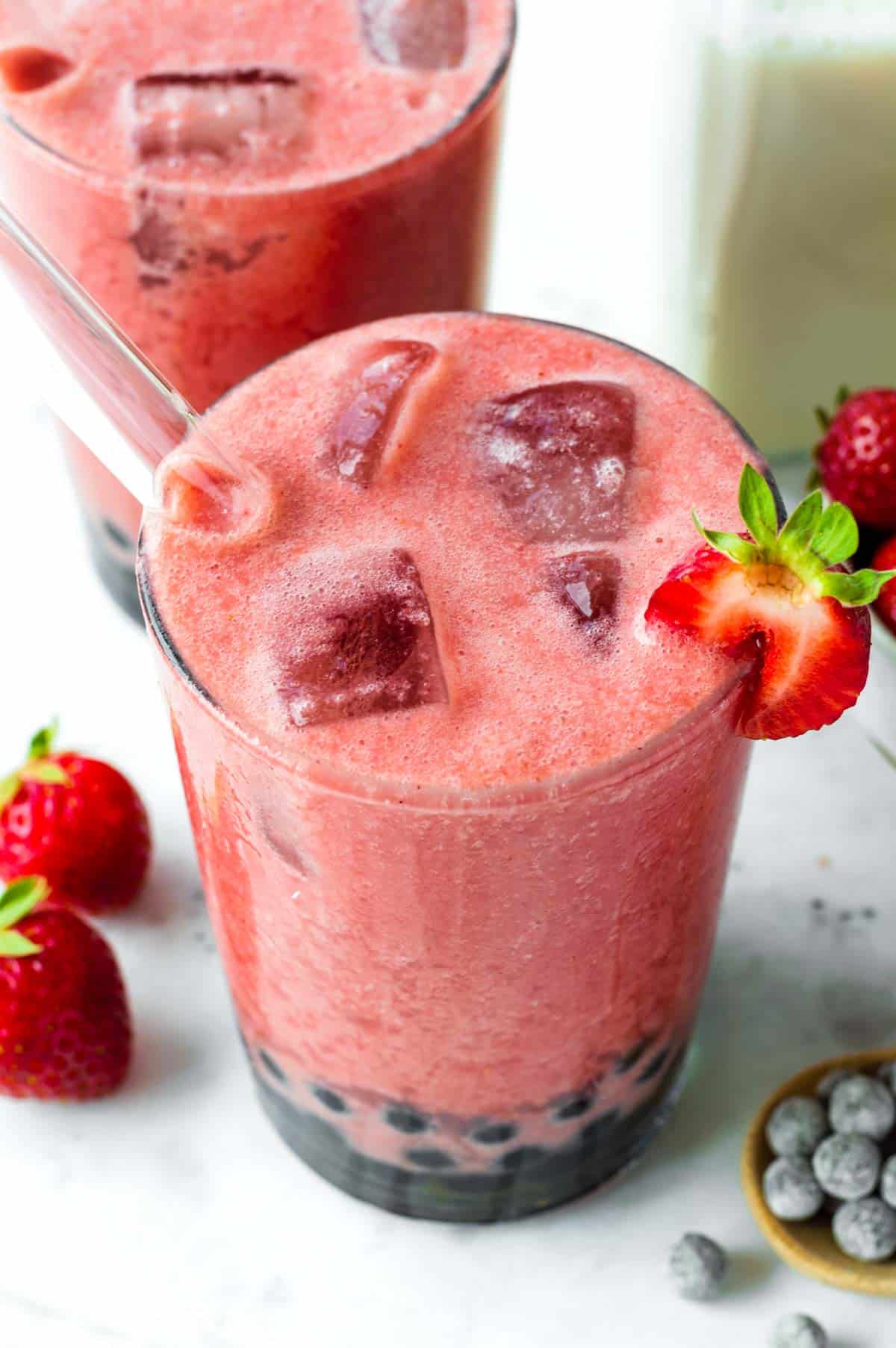 A glass filled with strawberry bubble tea, with a glass straw pointing out of it.