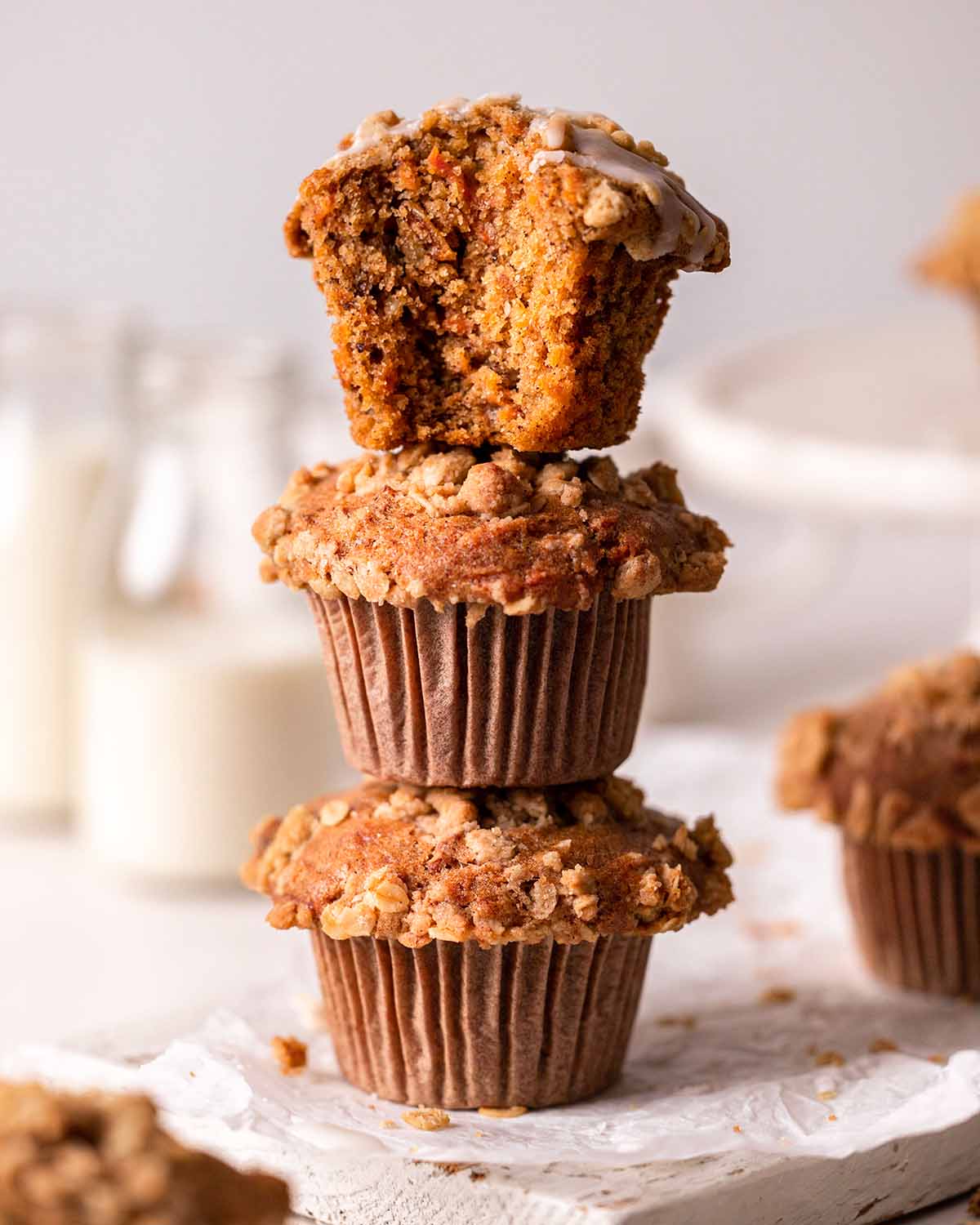 Three vegan carrot muffins stacked on one another with the top one missing a bite.