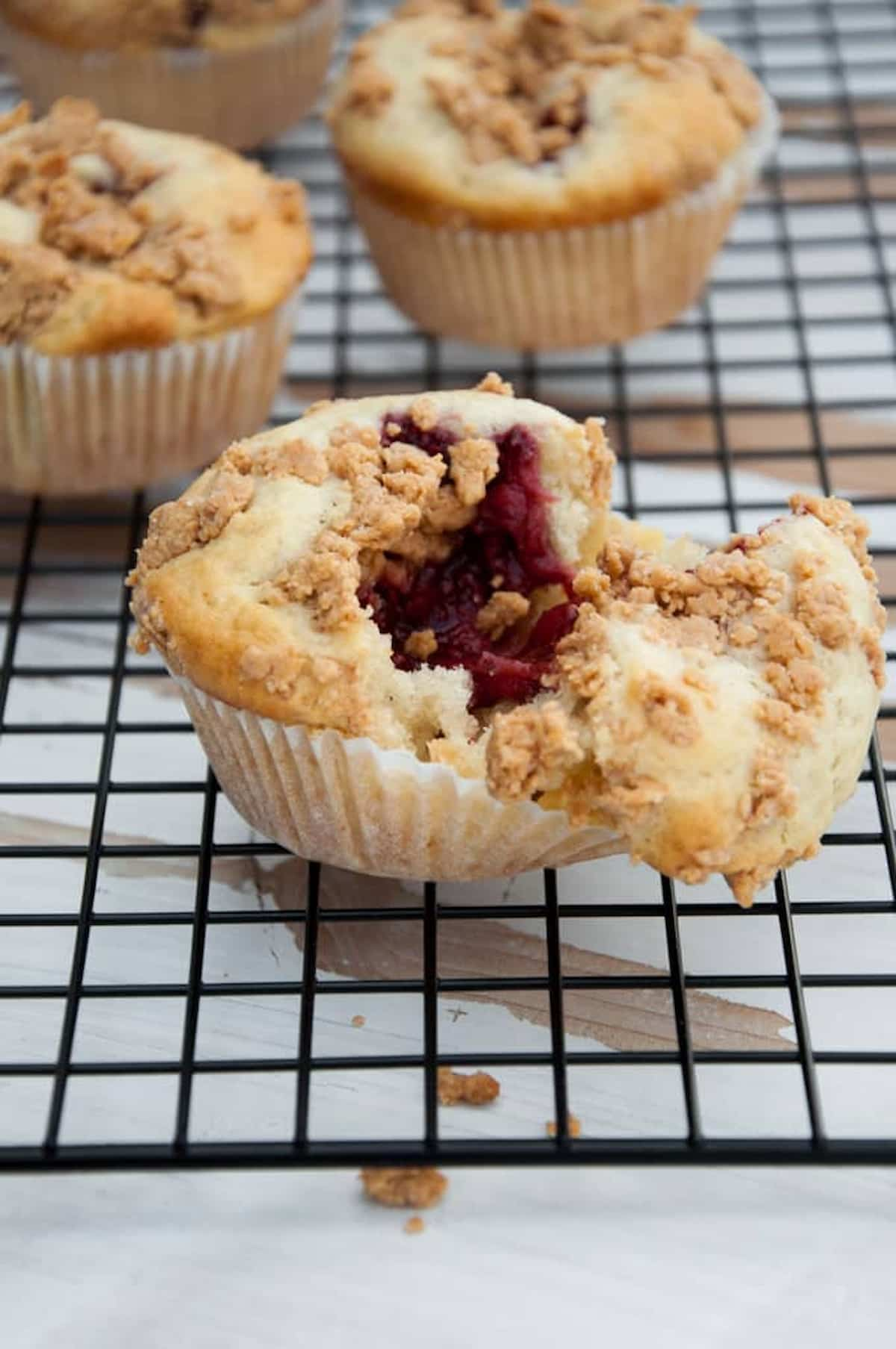 Vegan PB&J muffins on a cooling rack with one sliced open revealing a jam filling.