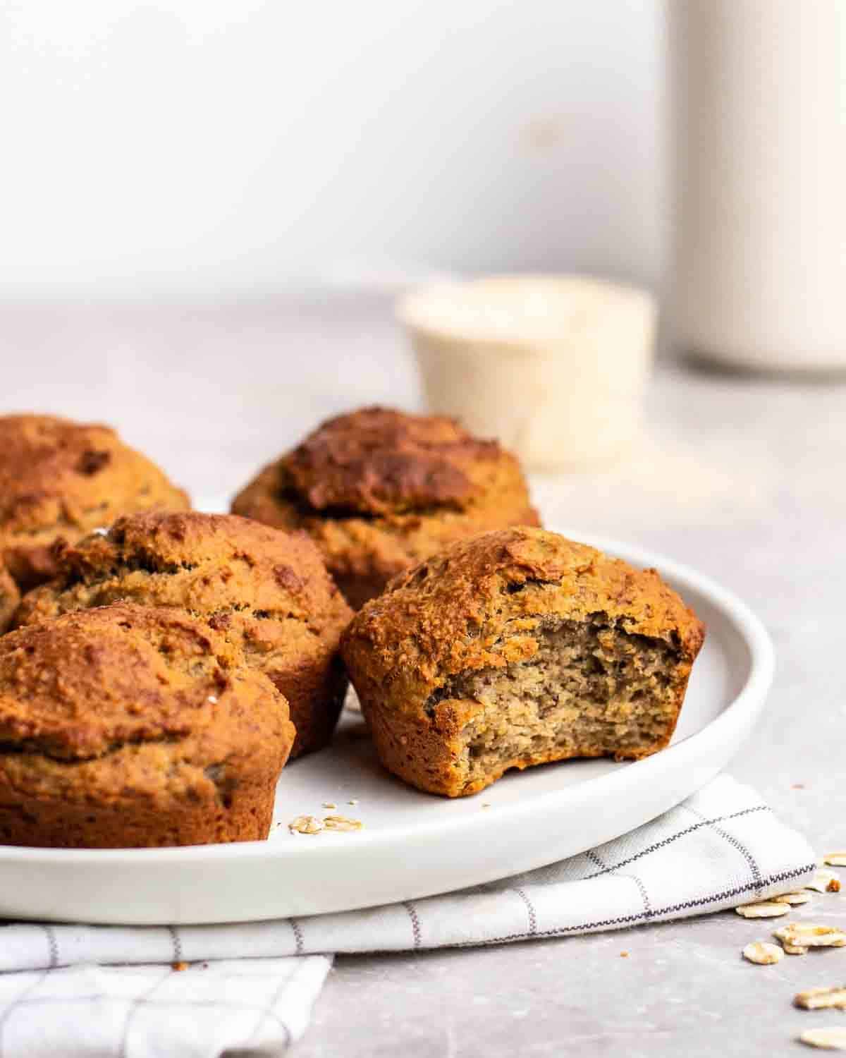 Vegan protein muffins on a plate with one muffin missing a bite out of it.