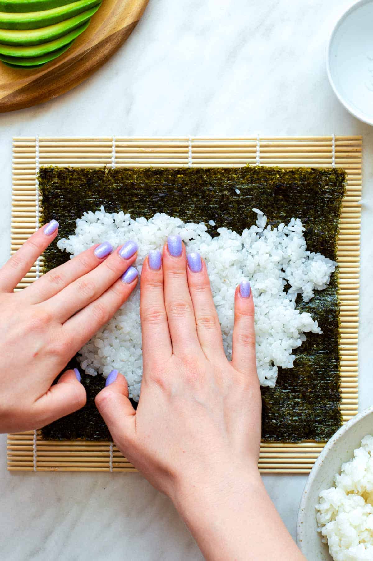Two hands pressing sushi rice on a sheet of nori.