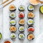 Avocado maki served on a marble board and topped with different toppings like sesame seeds and pickles ginger.