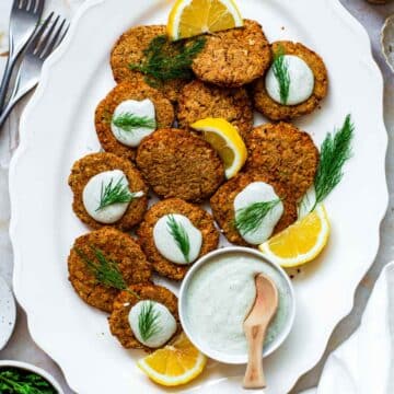 Chickpea patties served on a white platter, and topped with hemp aioli and fresh dill.