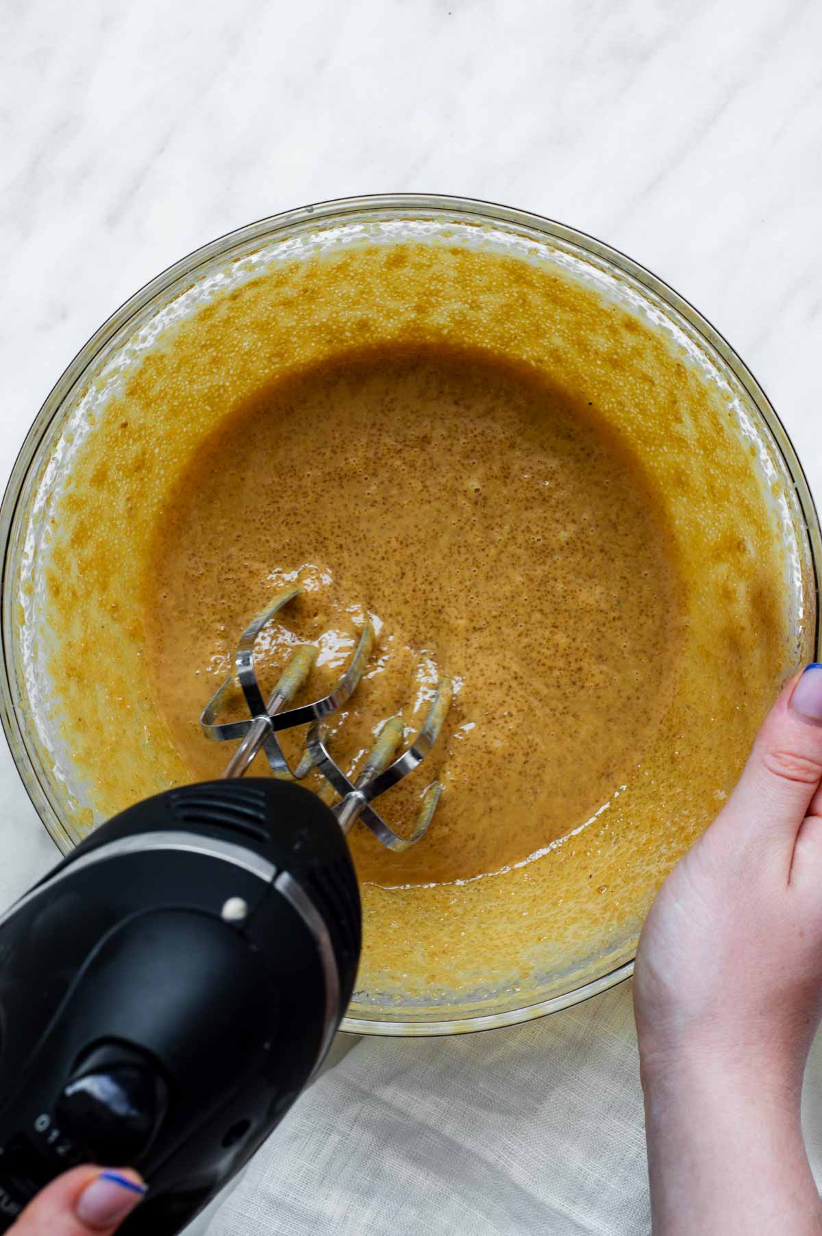 Mixing peanut butter and brown sugar in a glass bowl with a handheld mixer.