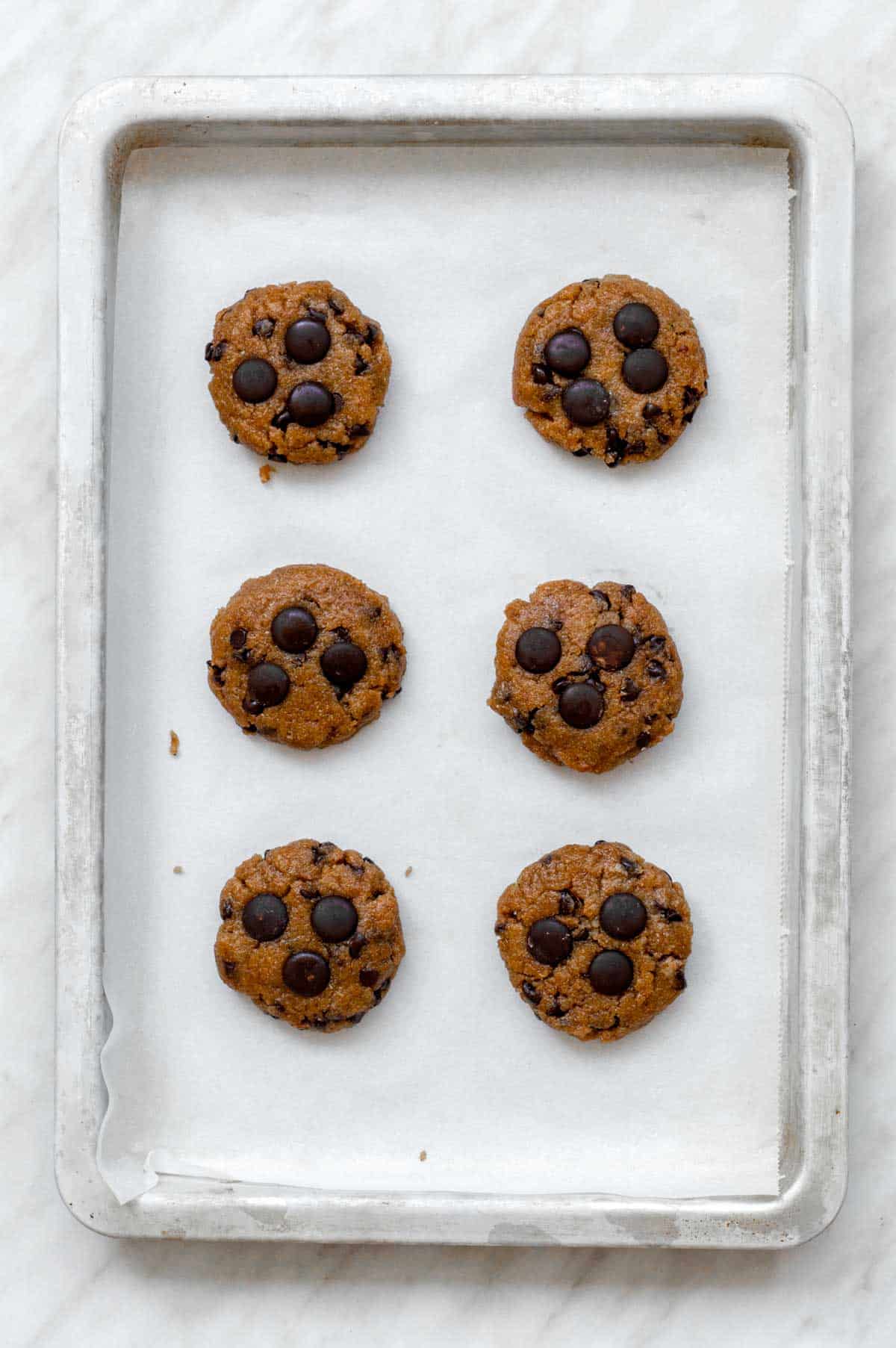 Six cookie dough balls placed on a baking sheet.