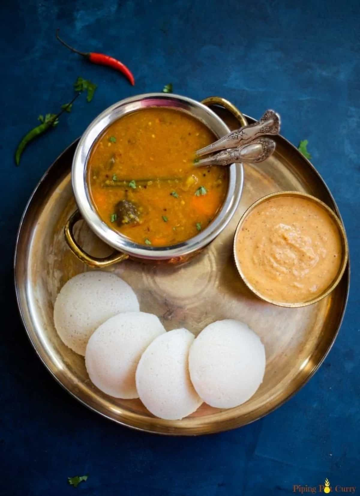 Steamed idli on a platter with a bowl of sauce and curry.