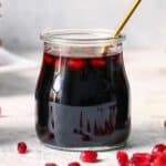 Pomegranate molasses in a glass jar with a spoon, and pomegranate perils scattered around.