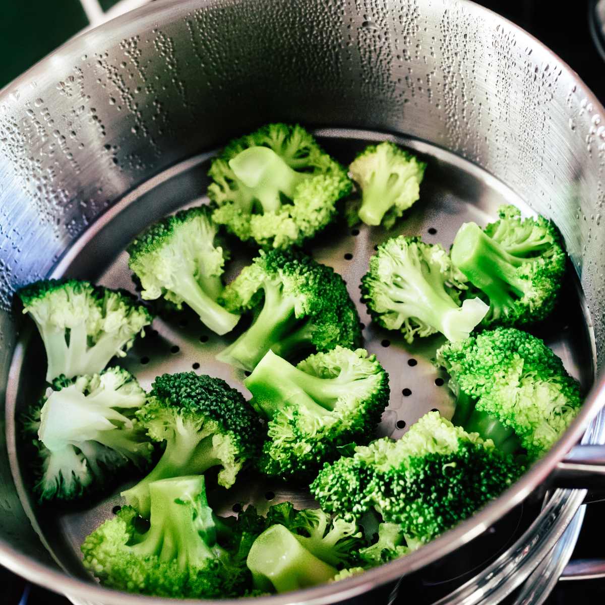 Steamed broccoli in a metal steamer basket.