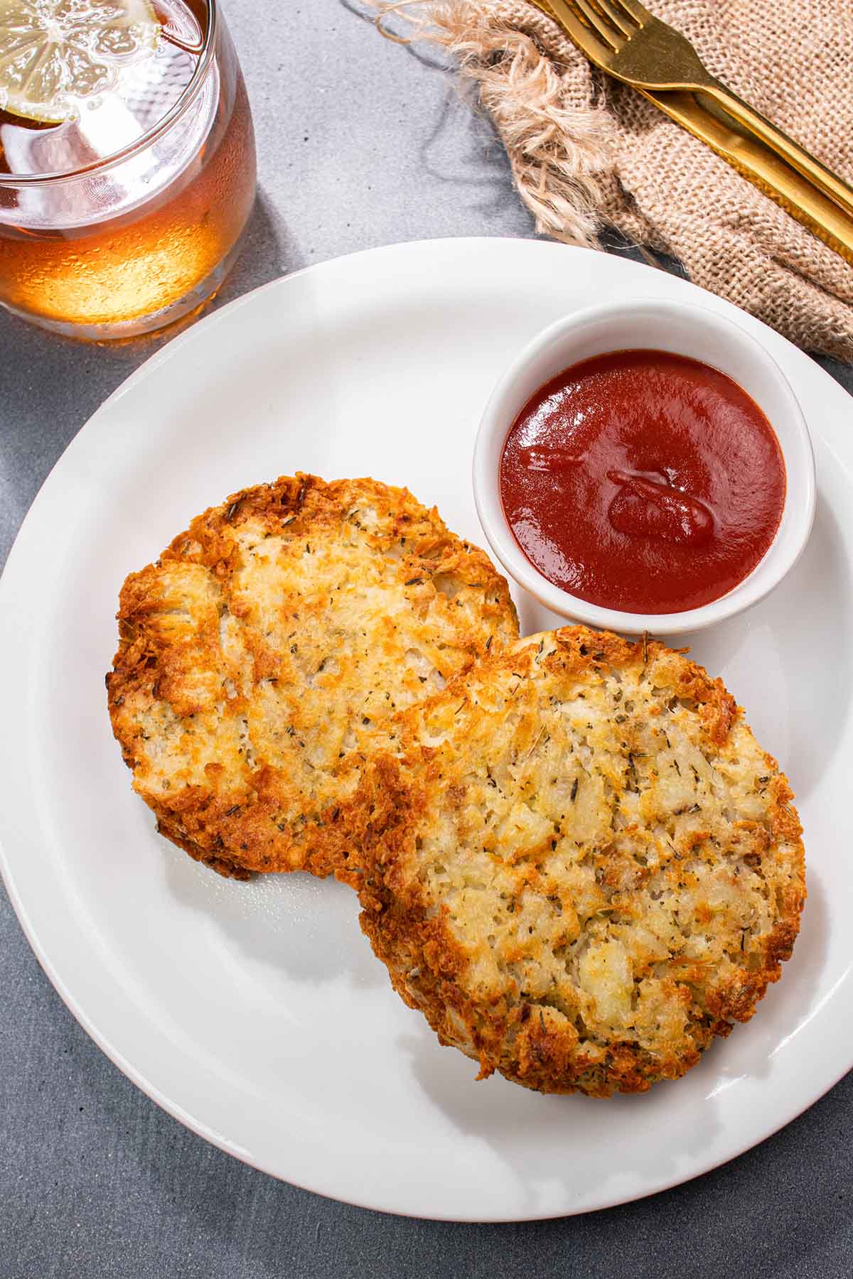 Two round hash browns on a plate, served with a side of ketchup.