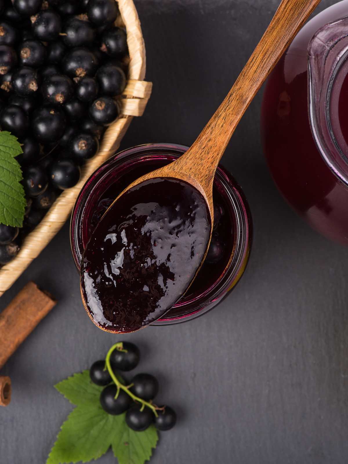 A spoonful of cassis syrup next to a basket of blackcurrants.