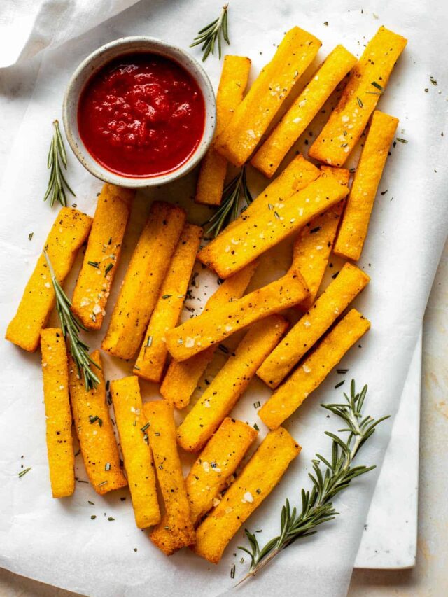 Polenta fries served next to a small bowl of marinara sauce and topped with flaky sea salt and rosemary.