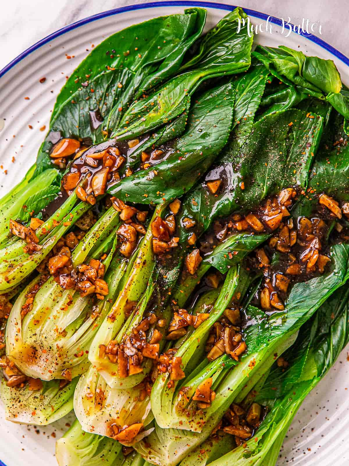 Steamed garlic bok choy on a plate topped with garlic.