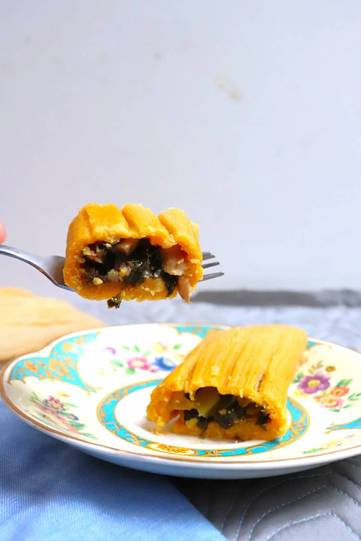 A tamale slice in half with a fork lifting one of the halves off the plate.