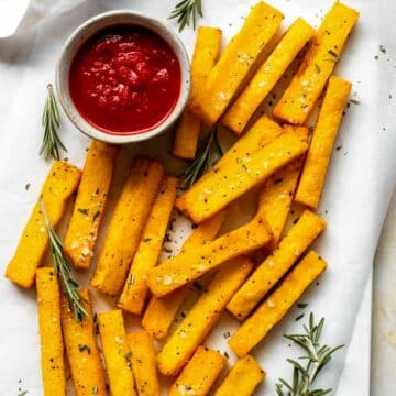 Polenta fries served next to a small bowl of marinara sauce and topped with flaky sea salt and rosemary.