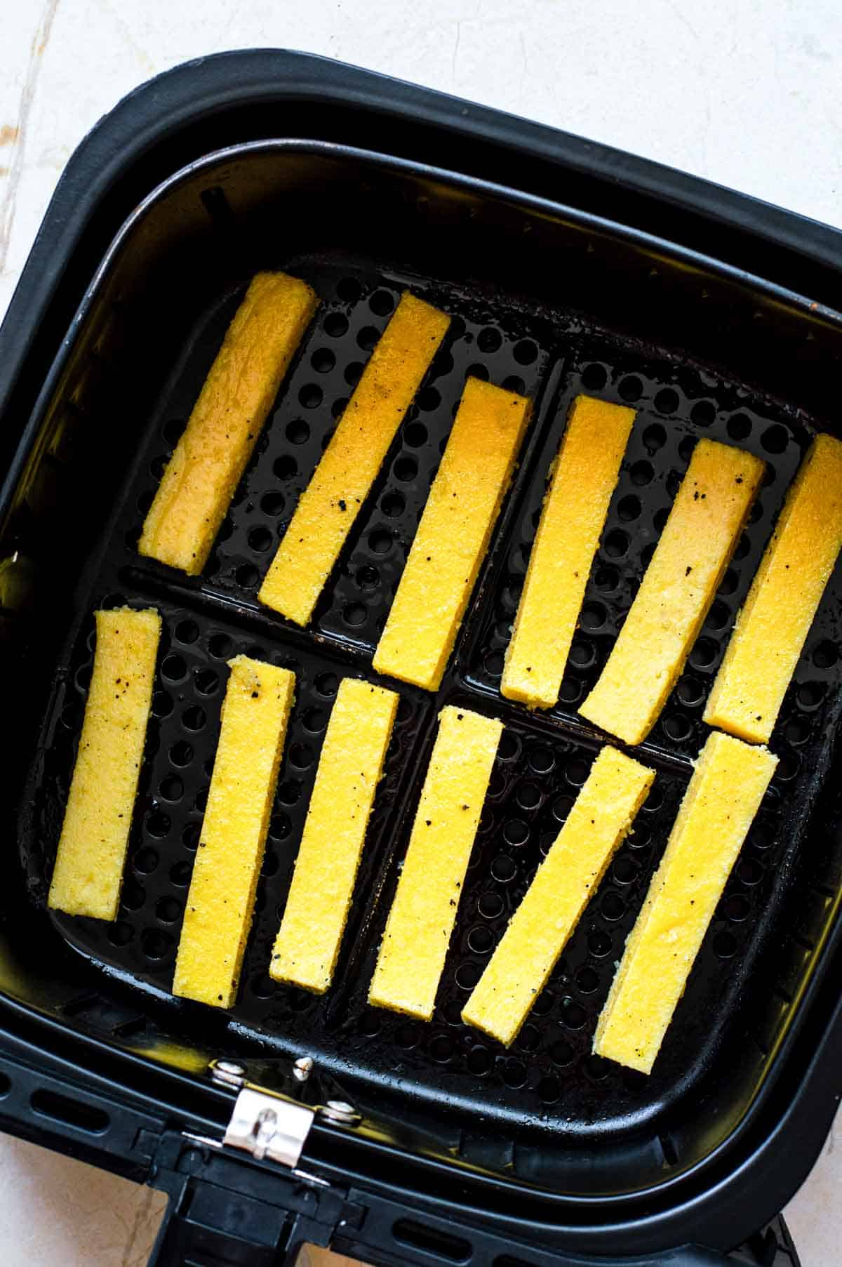 Uncooked polenta fritas in an air fryer basket.