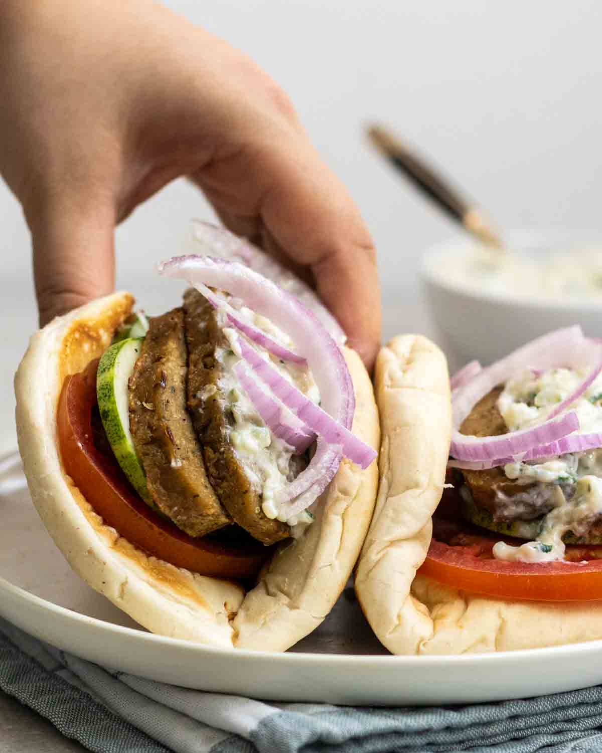 A hand reaching for a vegan seitan gyro on a plate.