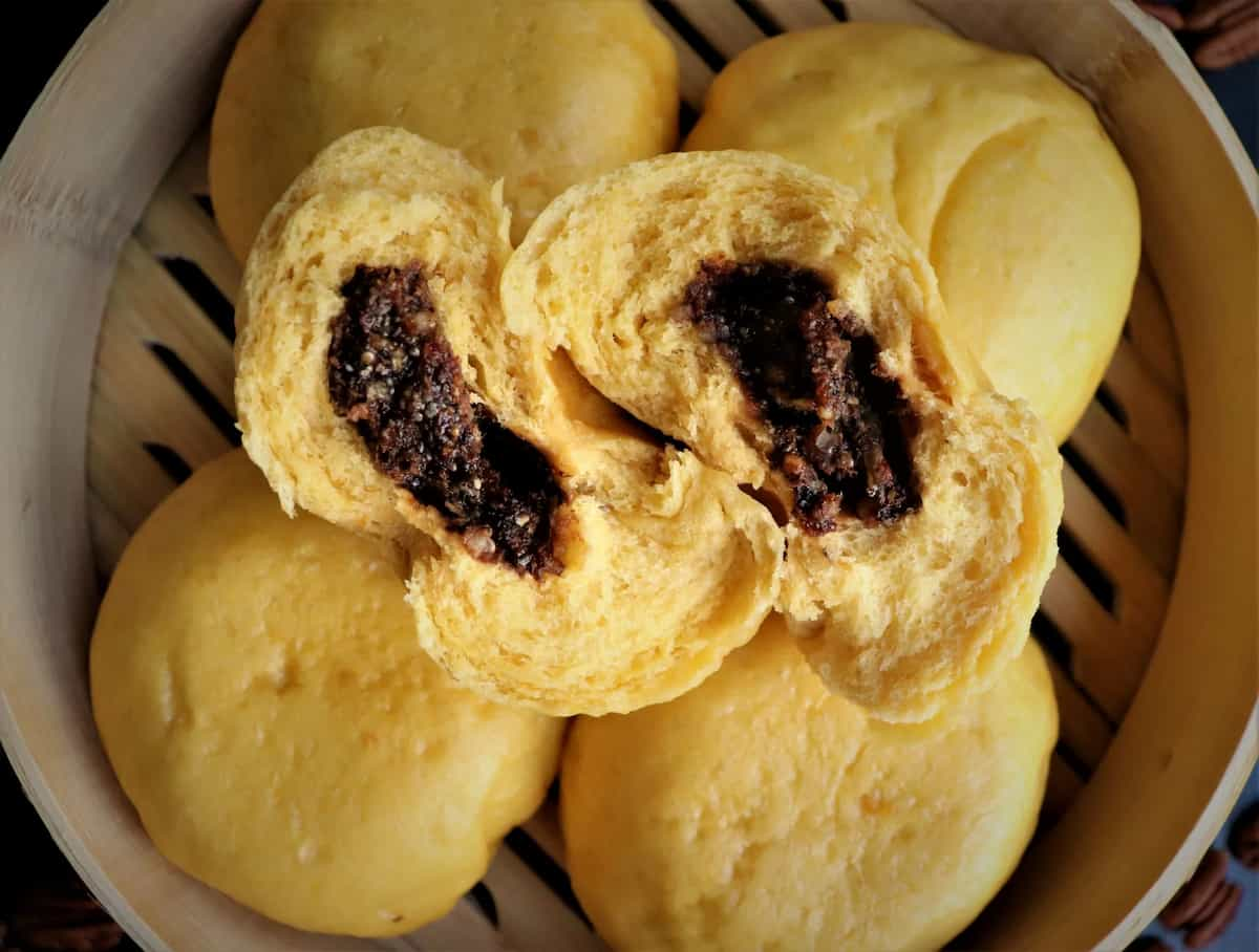 Sweet buns on steamer basket with one sliced in half showing the cut side.