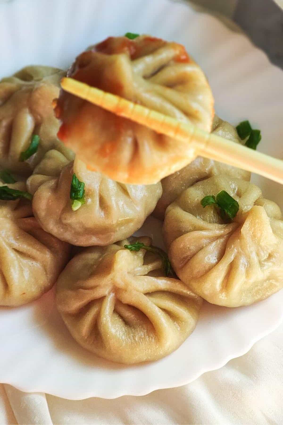 Momos on a plate with chopsticks holding one up.