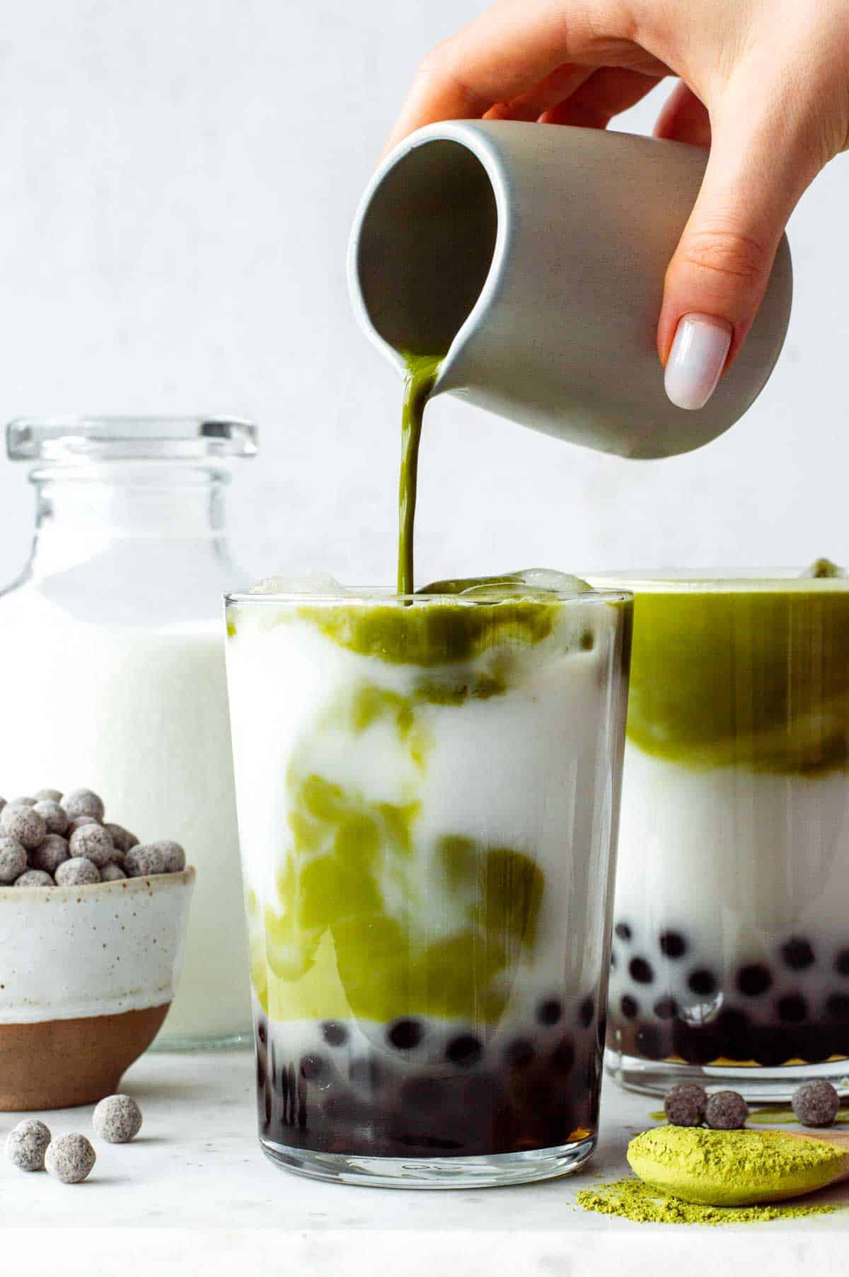 Pouring the matcha-milk mixture over the boba pearls in a glass.