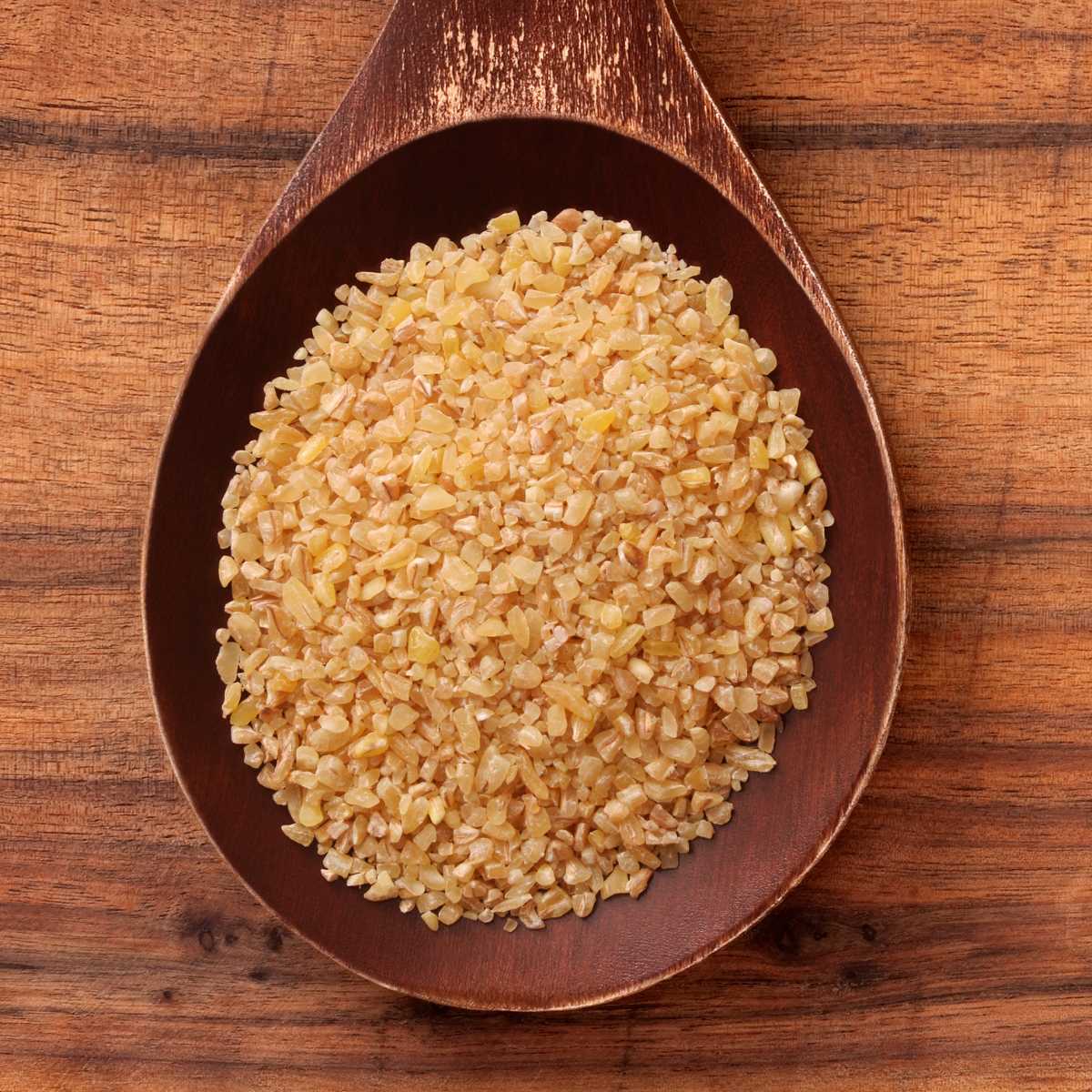 A wooden spoon holding dry bulgur wheat.