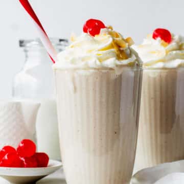 Two milkshake glasses filled with coconut shakes, topped with whipped cream and cherries.